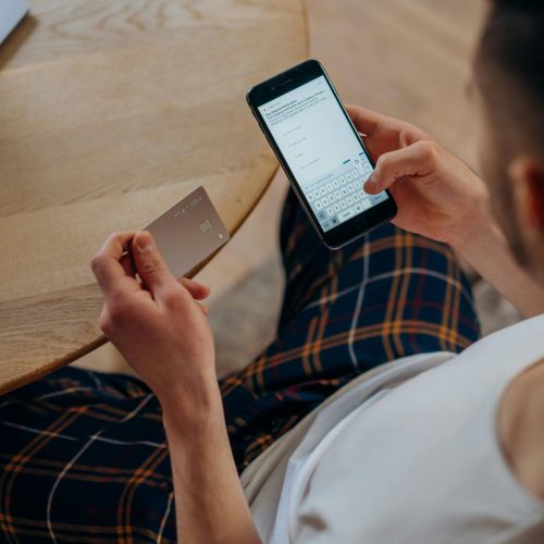 Adult male using a smartphone and credit card for online shopping while sitting indoors. Overhead view.